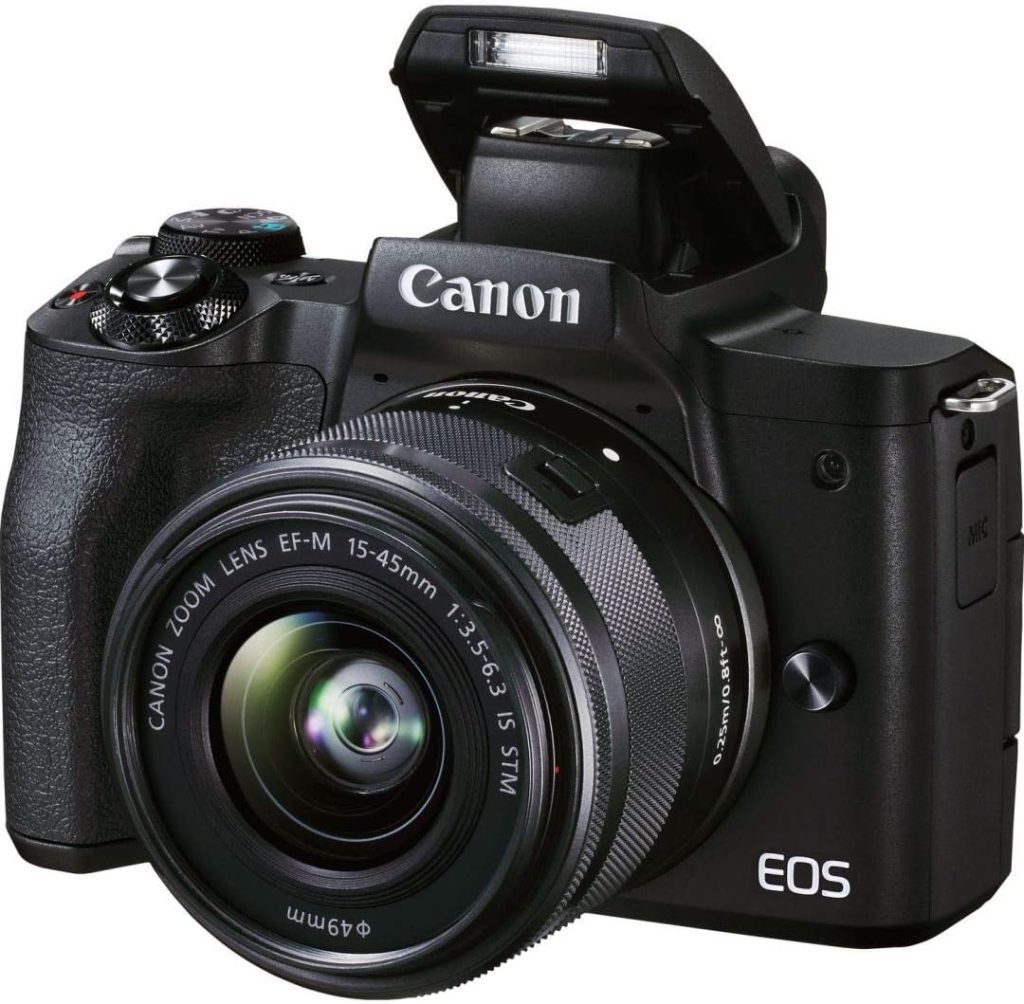 A three-quarter view of a black Canon EOS M50 Mark II mirrorless camera with a Canon EF-M 15-45mm lens attached and the built-in flash popped up.