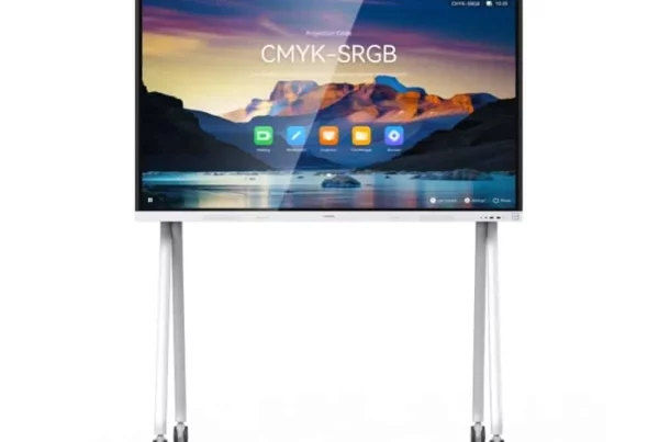 A front view of a large, white interactive display screen with a wide white bezel, mounted on a white mobile stand with four visible wheels. The screen displays a colorful landscape image with the text "CMYK-SRGB" centered on it. Below the text, there are several application icons, including a green "D" icon, a white brush icon, and a blue folder icon. A small camera is visible at the top center of the display's bezel.