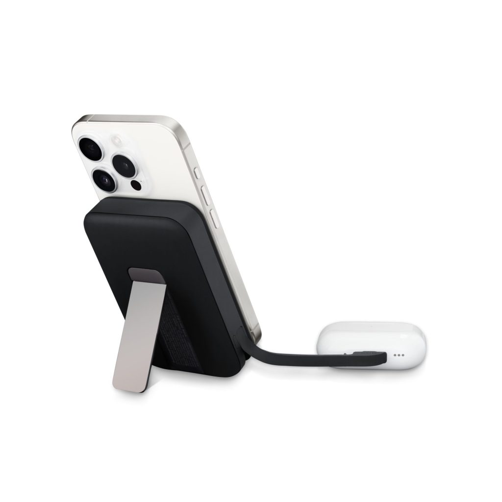 A black magnetic wireless power bank with a silver kickstand attached to the back of a silver iPhone, which is connected by a short black cable to white AirPods Pro charging case.