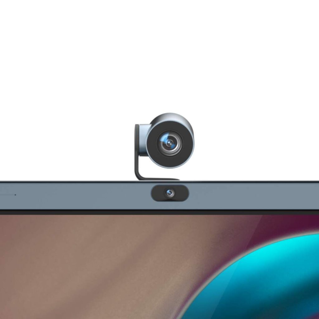 A black webcam is clipped to the top center of a laptop screen, with the laptop's built-in webcam visible directly below it. The screen displays a colorful, abstract background.