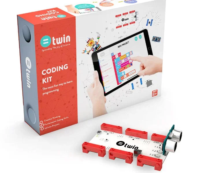 A "Twin Science Coding Kit" is displayed in an eye-level, slightly angled shot against a white background. The kit includes a large white box with a colorful graphic of hands interacting with a tablet displaying a block-based coding interface, and a smaller, red rectangular box nested within the larger one. The red box is labeled "@twin Coding Kit: The most fun way to learn programming," and lists "Creative Thinking," "Fundamental Coding Skills," and "Infinite Projects." In the foreground, a white circuit board with red connectors and two ultrasonic sensors is visible. The large white box also has an "AGES 8+" label.