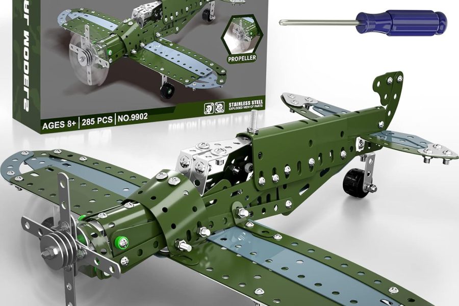 A metal construction toy kit of a green and gray airplane is displayed with its packaging and tools against a white background. The assembled airplane model, featuring an olive green fuselage and wings with light gray undersides and silver accents, is prominent in the foreground. A propeller is at the front, and black wheels are visible underneath. In the background, the kit's dark green box is shown, labeled "METAL MODELS" and "BUILD YOUR OWN FIRST ASSEMBLED AIRPLANE." The box also indicates "AGES 8+," "285 PCS," and "NO.9902," and mentions "STAINLESS STEEL." Above the box, a silver wrench and a blue-handled screwdriver, the tools used for assembly, are laid out.