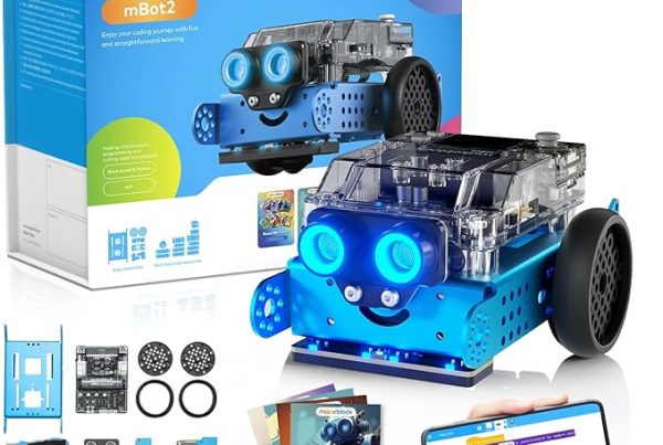 A blue makeblock mBot2 robot kit is displayed against a white background, accompanied by its packaging and various components. The assembled blue robot, with clear top casing and two large glowing blue "eyes," is prominent in the foreground. Behind it is the white and blue retail box, which features an image of the robot and details like "mBot2" and "Enjoy your coding journey with fun and straightforward learning." In the bottom left, an array of disassembled robot parts, including blue metal plates, wheels, and circuit boards, are laid out. Below the robot in the foreground, a smartphone screen shows a colorful coding interface, with a hand pointing to it. To the left of the phone, an instruction booklet with a robot illustration on its cover is also visible.
