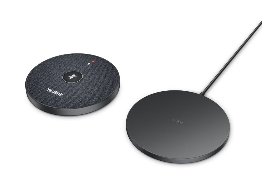 A top-down shot shows a round, dark gray Yealink microphone speaker on the left, next to a slightly larger, flatter, round, dark gray wireless charging pad on the right, both resting on a light gray surface.