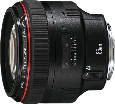 A high-quality product shot of a black Canon EF 85mm f/1.2L II USM lens on a white background. The lens is shown from a side angle, with the red L-series ring and the focus distance window clearly visible. The focus ring and AF/MF switch are also prominent.