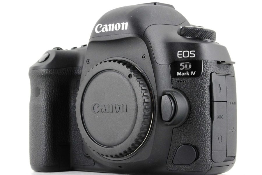 A front and side angled shot of a black Canon EOS 5D Mark IV DSLR camera body with the lens mount cap on. The camera has a textured grip on the right side and the "Canon" and "EOS 5D Mark IV" logos are clearly visible. The background is a solid white.