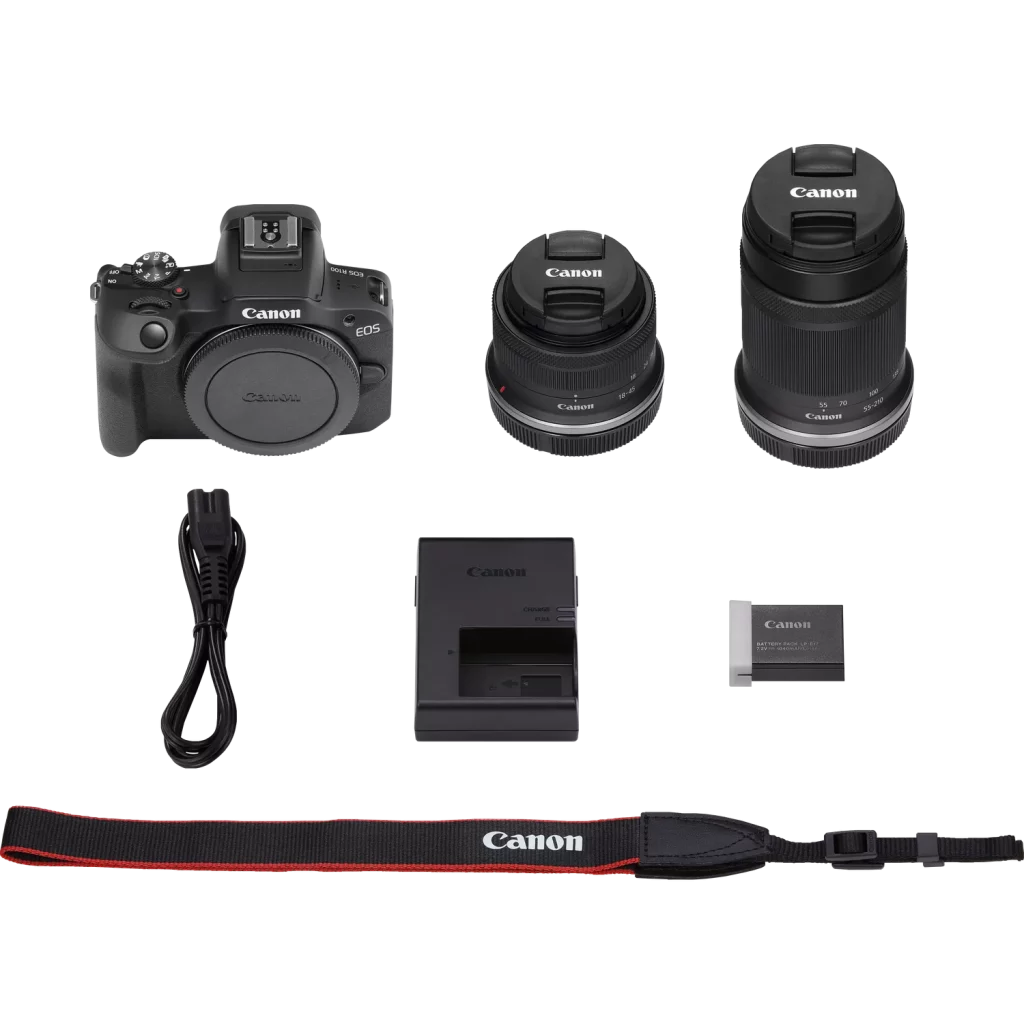 A flat-lay product shot of the Canon EOS R100 camera kit. The items are arranged in three rows on a white background. The top row shows the camera body on the left and two lenses with lens caps on the right. The middle row contains the power cord, battery charger, and battery. The bottom row displays the camera's strap.